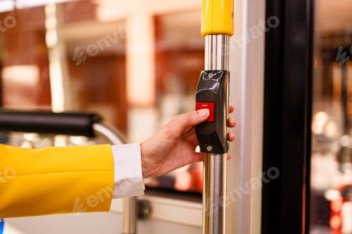 Preview: Unrecognizable woman's hand pressing stop button on city bus. Concept of commuting.