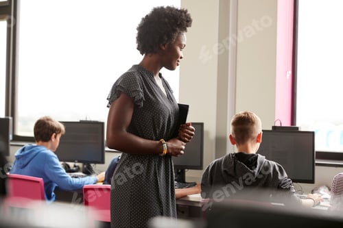 Preview: Female Teacher Supervising Line Of High School Students Working at Screens In Computer Class