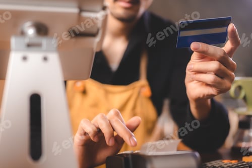Preview: Closeup of young Asian barista wearing an orange apron uniform filling bank debit and credit card