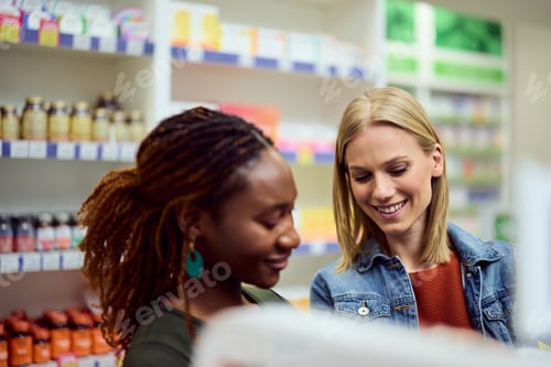 Preview: Two Women Smiling in Pharmacy While Browsing Medicine and Health Products
