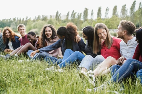 Preview: Multiethnic friends having fun sitting on grass outdoor - Focus on right girl face
