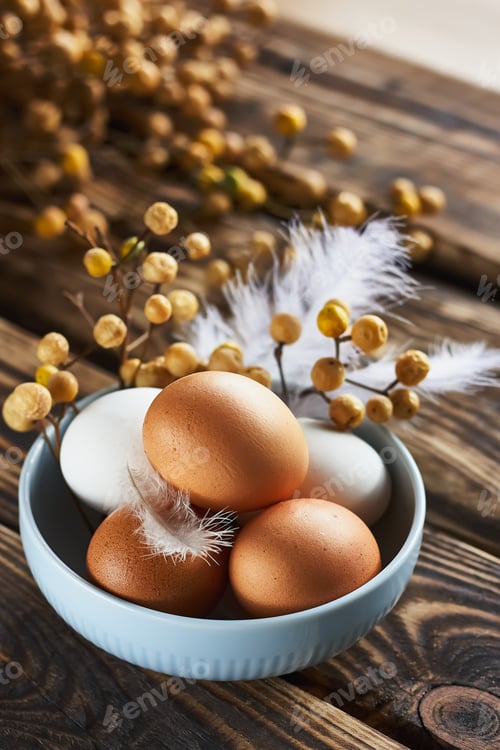 Preview: White and brown easter eggs with feather in a bowl on dark wooden table.