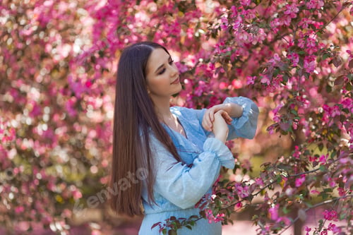 Preview: Cute of girl is standing near a blooming apple tree