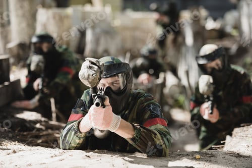 Preview: selective focus of concentrated paintball player in protective mask aiming with marker gun and his