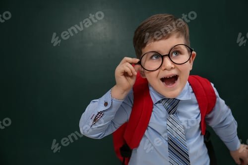 Preview: Funny little child wearing glasses near chalkboard, space for text. First time at school