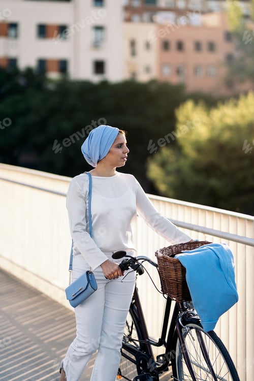 Preview: Muslim woman walking with her bicycle next to her on the footbridge