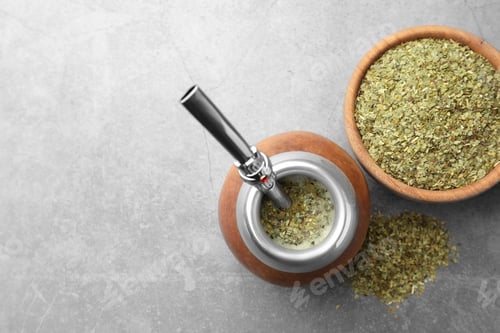 Preview: Calabash with bombilla and bowl of mate tea leaves on grey table, flat lay. Space for text
