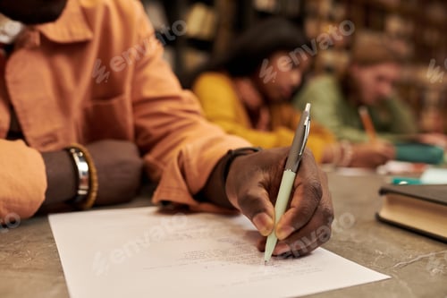 Preview: Young Black Man Writing Exam Paper in Library with Focused Students