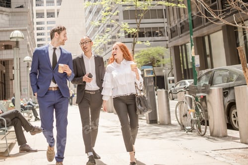 Preview: Young businesswoman and businessmen with takeaway coffee strolling along sidewalk, New York, USA