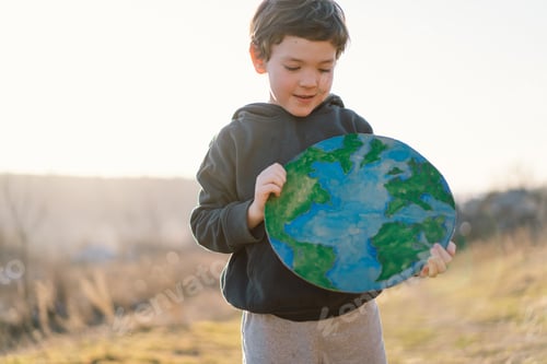 Preview: Little boy holding planet in hands against green spring background. Earth day
