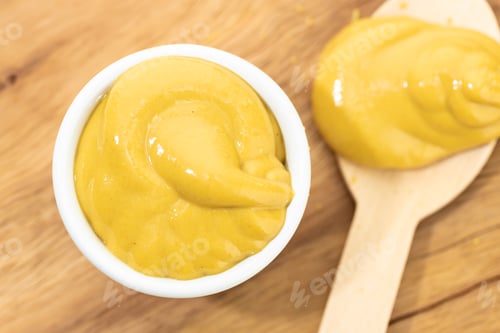 Preview: Top view of Mustard sauce in bowl and spoon on wooden table