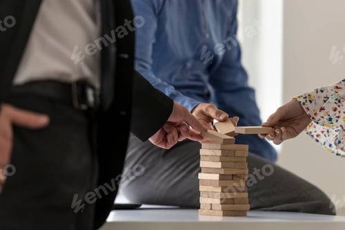 Preview: Group of colleagues in an office carefully building a tower of w