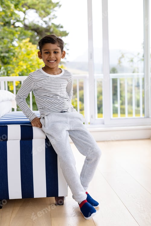 Preview: Portrait of happy biracial boy wearing pyjamas in bedroom in front of window with view of garden