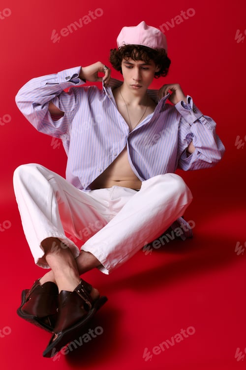 Preview: Young man showcases unique style against vibrant red backdrop in a creative setting