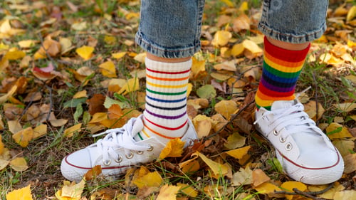Preview: a child in sneakers and mismatched socks stands on yellow autumn leaves.