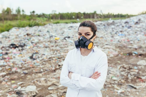 Preview: Female scientist in a protective respirator mask at a landfill assesses the level of environmental