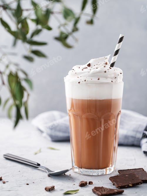Preview: Hot chocolate with whipped cream and chocolate pieces in a glass on a blue background with a branch