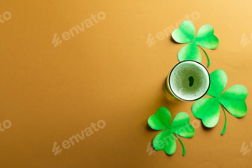 Preview: Image of glass with green beer, clover and copy space on orange background