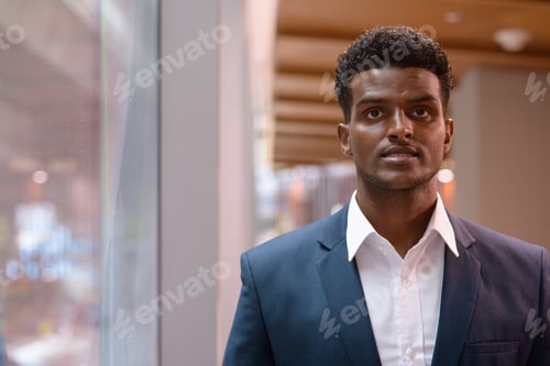 Preview: Portrait of African businessman standing next to window indoors while looking at camera