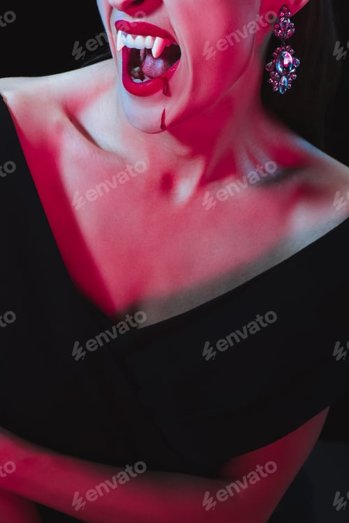 Preview: cropped view of vampire woman showing her vampire fangs on dark background