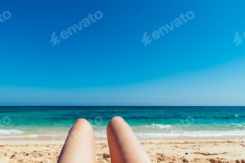 Preview: Close up of mature woman legs sunbathing on the beach against blue sea background