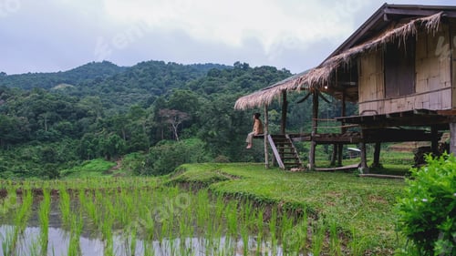 Preview: A woman sitting on wooden hut balcony in greenery rice terraces on cloudy day
