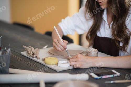 Visualização: Jovem mulher em uma aula de cerâmica trabalhando com ferramentas diferentes