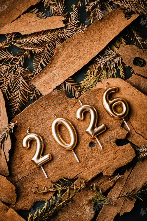 Visualização: Velas douradas de 2026 apoiadas em madeira rústica e vegetação para celebração