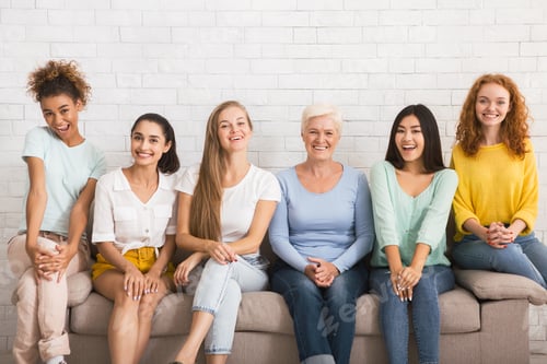 Preview: Smiling Diverse Women Sitting On Sofa Over White Brick Wall