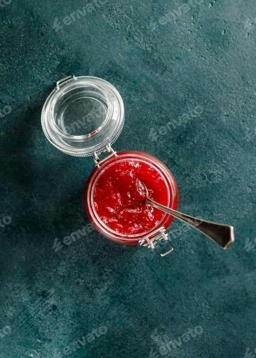 Preview: Top view of strawberry jam in a glass jar on a green background.