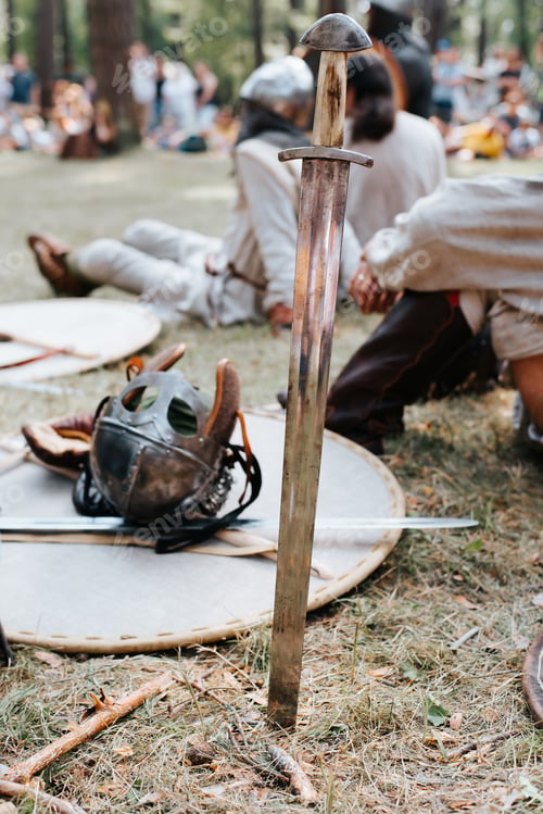 Preview: Close-up of a medieval old steel sword stuck in the ground, selective focus