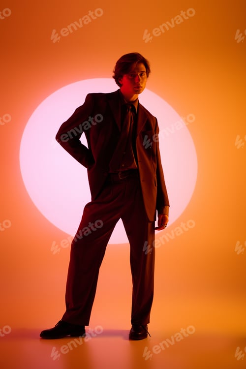 Preview: Young stylish man posing confidently against a vibrant orange backdrop with a glowing circle