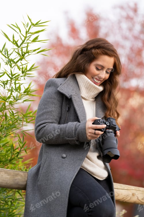Preview: Young woman looking at her photo camera and smiling in a park