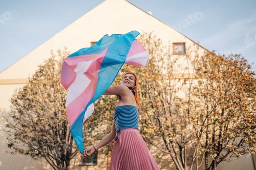 Preview: Young woman waving transgender pride flag in the city