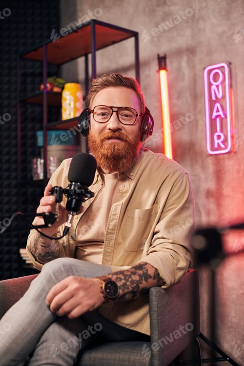 Preview: cheerful handsome man with red hair and beard with headphones looking at camera during podcast