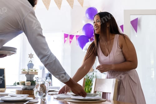 Preview: Smiling woman setting table for bar mitzvah with festive decorations