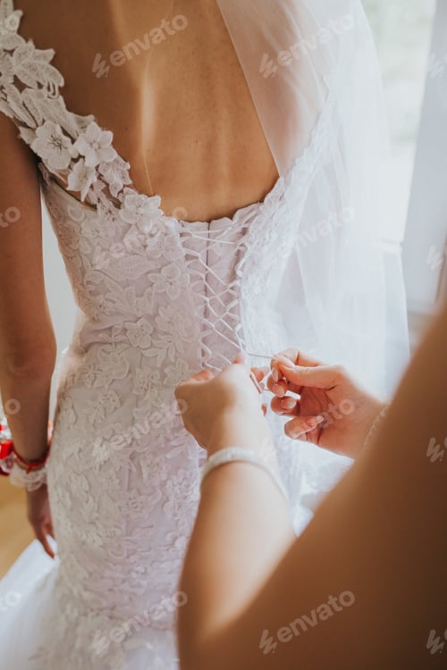 Preview: Vertical shot of a female's hands tying the threads of the bride's dress