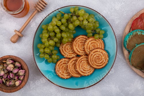 Preview: top view cookies with green grapes on a blue plate with honey and dried buds on a white background