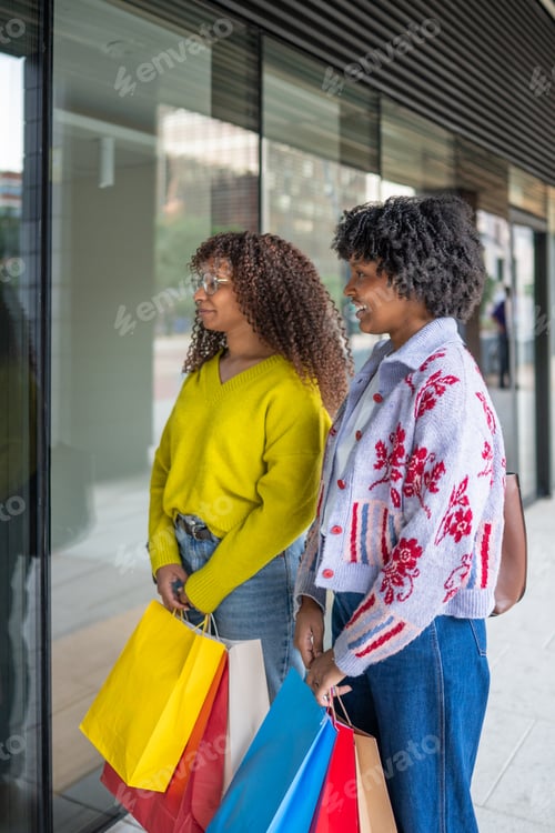Preview: Two women window shopping while holding colorful bags