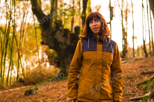 Preview: Lifestyle, a young woman in a yellow jacket walking backwards along a forest