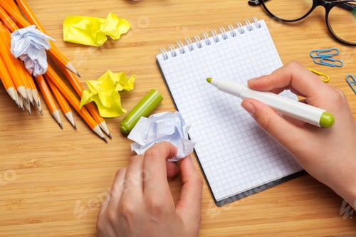 Preview: White note pad on a wooden table. Around the notepads lies lot crumpled paper