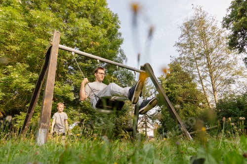 Preview: A father swings joyfully while his child watches with delight at a local playground