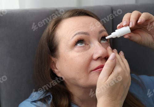 Preview: Woman applying eye drops on bed at home