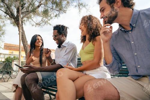 Preview: Group of friends laughing while watching something on smartphone outdoors