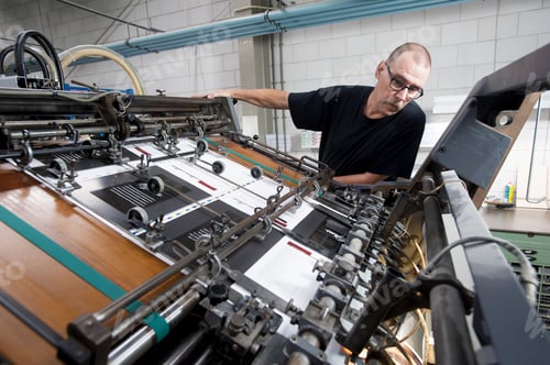 Preview: Worker monitoring print machine in printing workshop