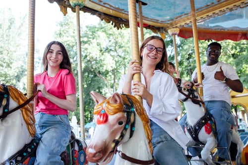 Preview: Group of young friends enjoying a carousel ride on colorful horses