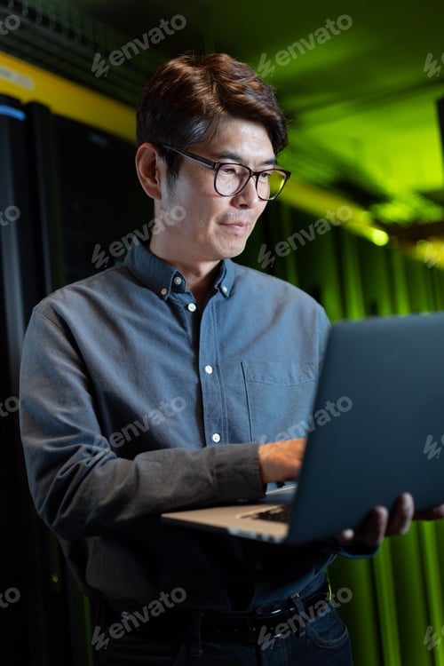 Preview: Asian male engineer using laptop in computer server room