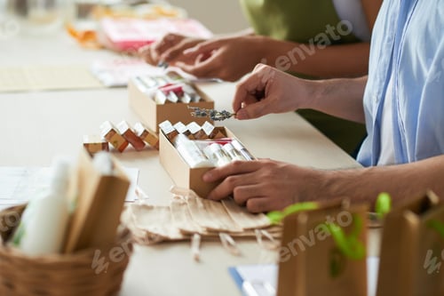 Preview: Hands of people putting handmade soap in boxes and decorating with lavender branches