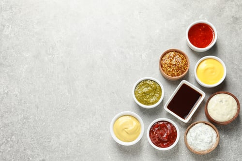 Preview: Set of different delicious sauces on grey table, top view. Space for text