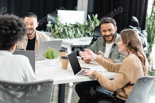 Preview: cheerful interracial colleagues using laptops and planning project together in modern coworking